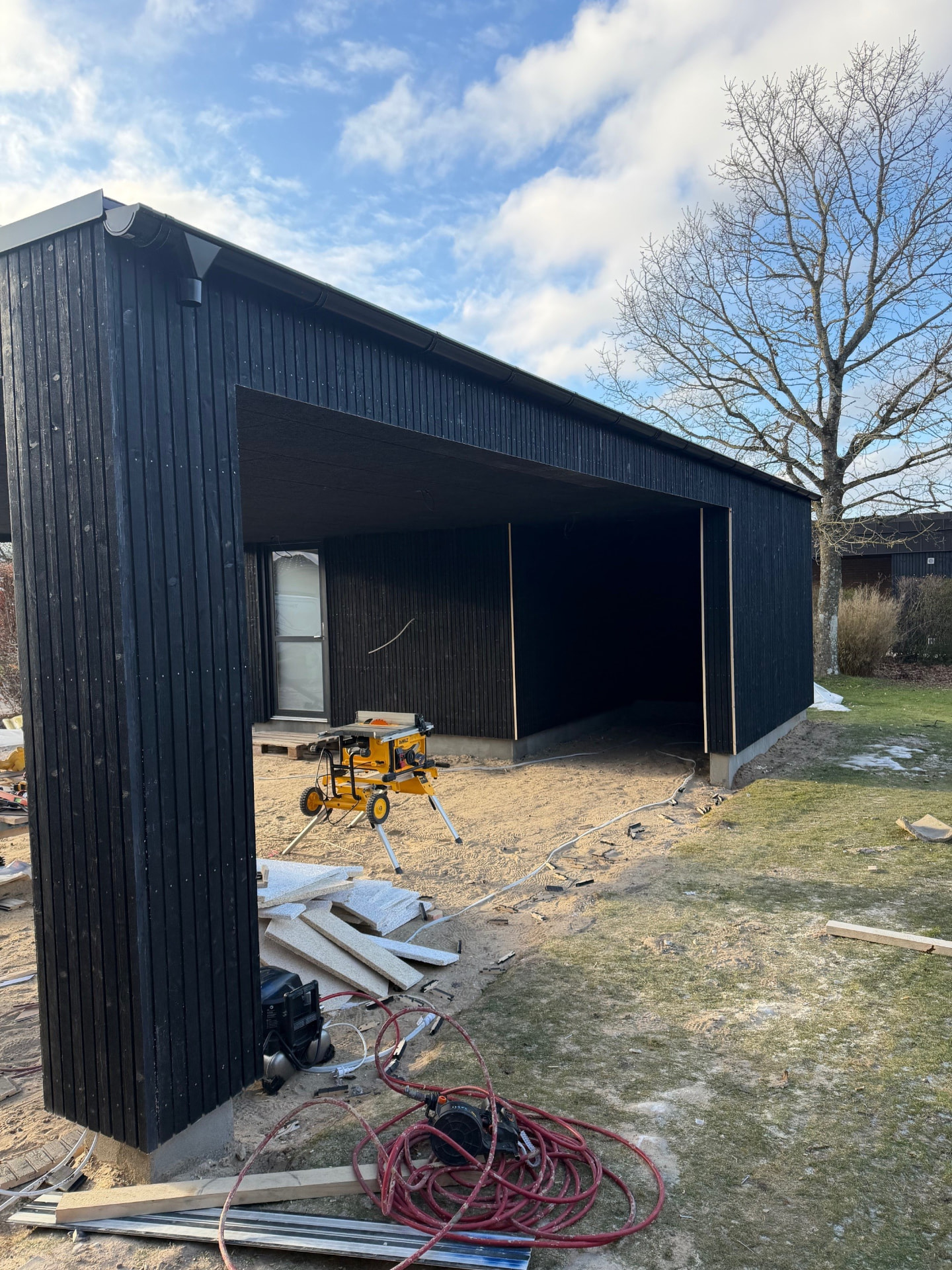 Carport med redskabsskur og mørk træbeklædning under opførelse i Vestbjerg